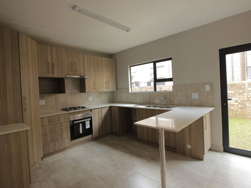 Modern kitchen featuring wood-finish cabinetry, stone countertops, built-in gas hob, electric oven, and a breakfast bar with direct access to the rear garden.