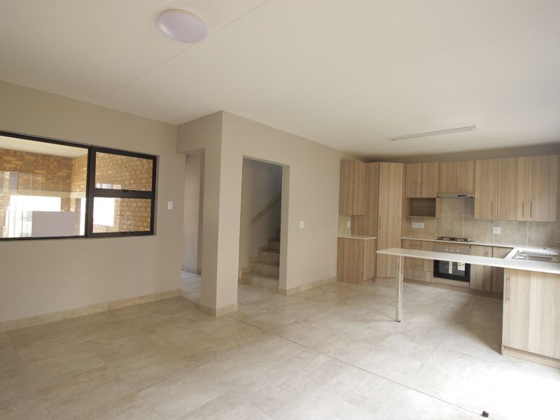 Spacious open-plan kitchen and living area featuring modern light wood cabinetry, built-in appliances, and neutral tiled flooring throughout.