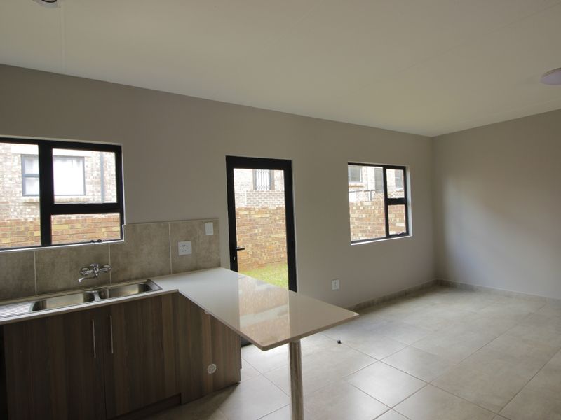 An open-plan living and kitchen area featuring tiled flooring, modern cabinetry with stone countertops, and direct access to the rear exterior.