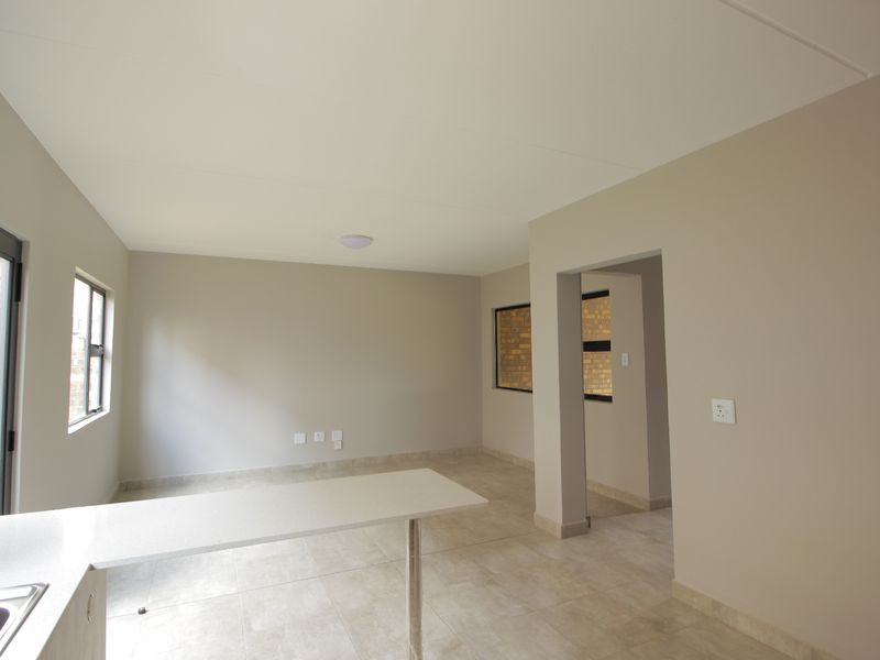 An open-plan living and kitchen area featuring neutral wall tones, tiled flooring, and a functional breakfast counter in a clean, vacant space.