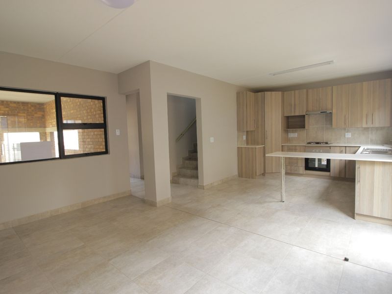 Spacious open-plan living and kitchen area featuring modern light wood cabinetry, built-in appliances, tiled flooring, and direct access to the staircase.
