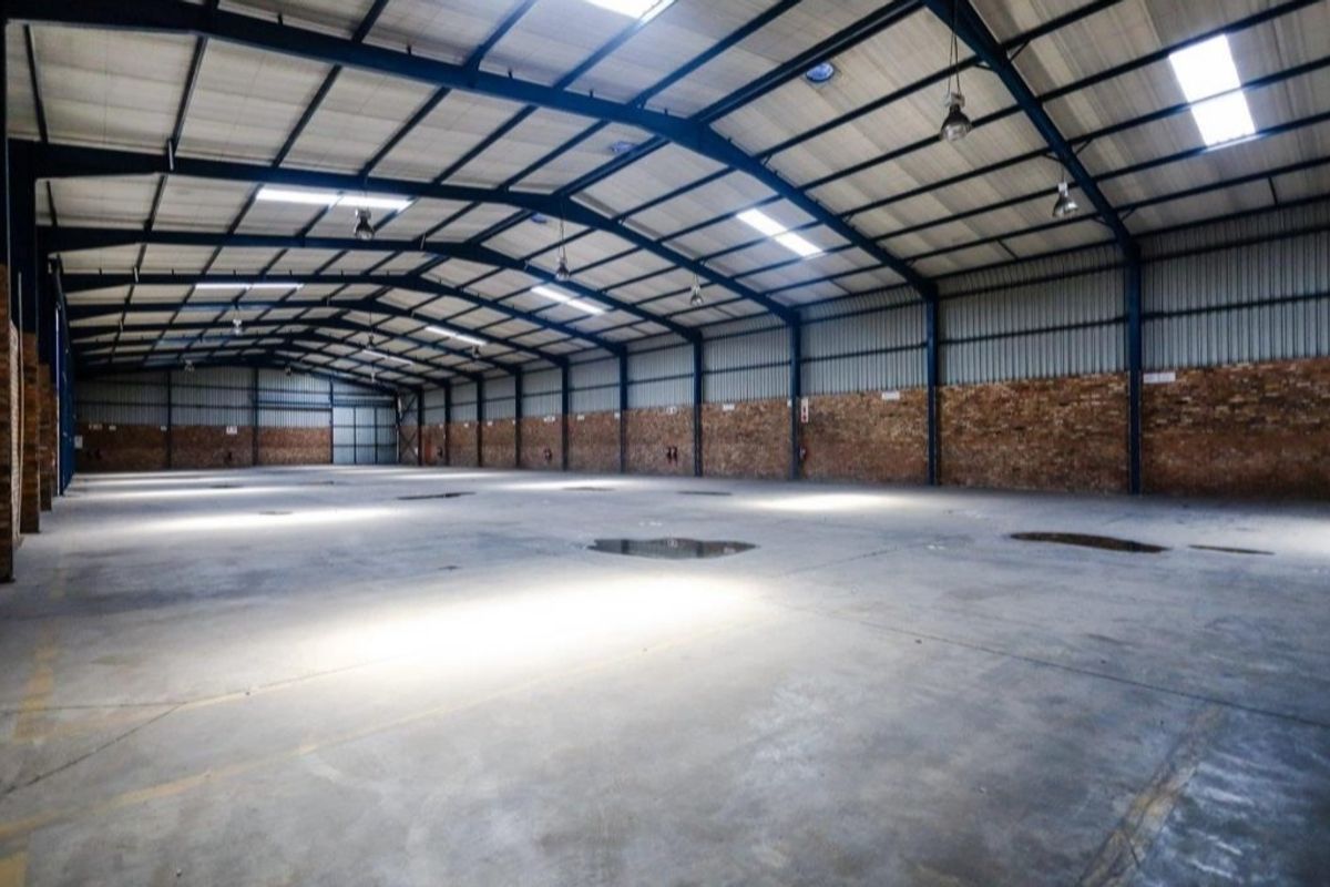 Spacious industrial warehouse featuring exposed steel portal framing, high ceilings with integrated skylights, durable concrete flooring, and exposed brick wall finishes.