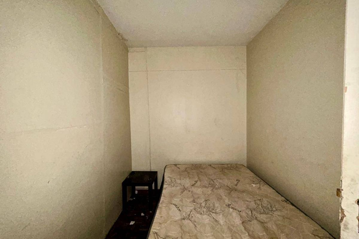A small bedroom space requiring significant cosmetic updates, including wall repairs and flooring replacement to improve the overall condition.