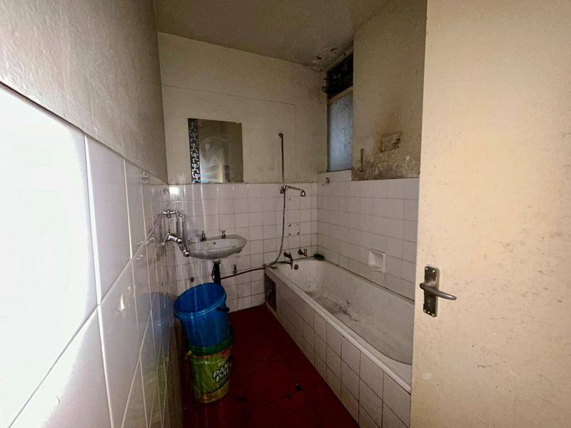 A dated bathroom featuring a bathtub, wall-mounted basin, and tiled finishes, currently in need of significant renovation and cosmetic repair.