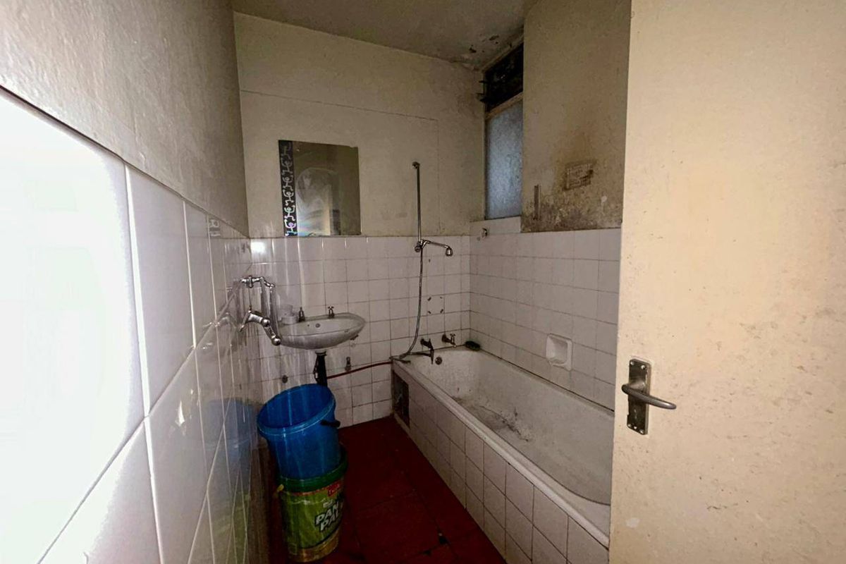 A dated bathroom featuring a bathtub, wall-mounted basin, and tiled finishes, currently in need of significant renovation and cosmetic repair.