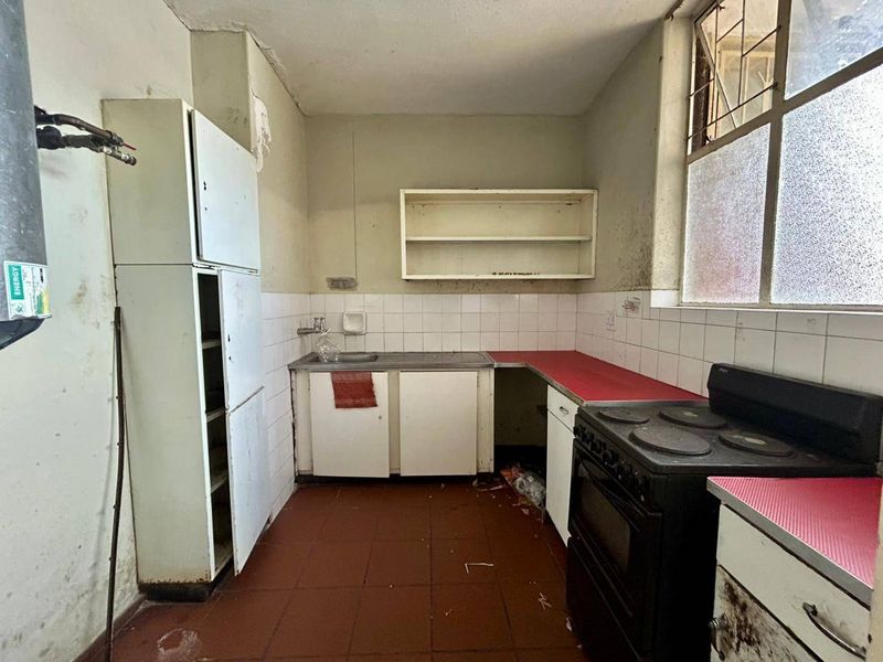 A dated kitchen featuring original cabinetry, a stainless steel sink, and an electric stove, requiring significant renovation and cosmetic updates.