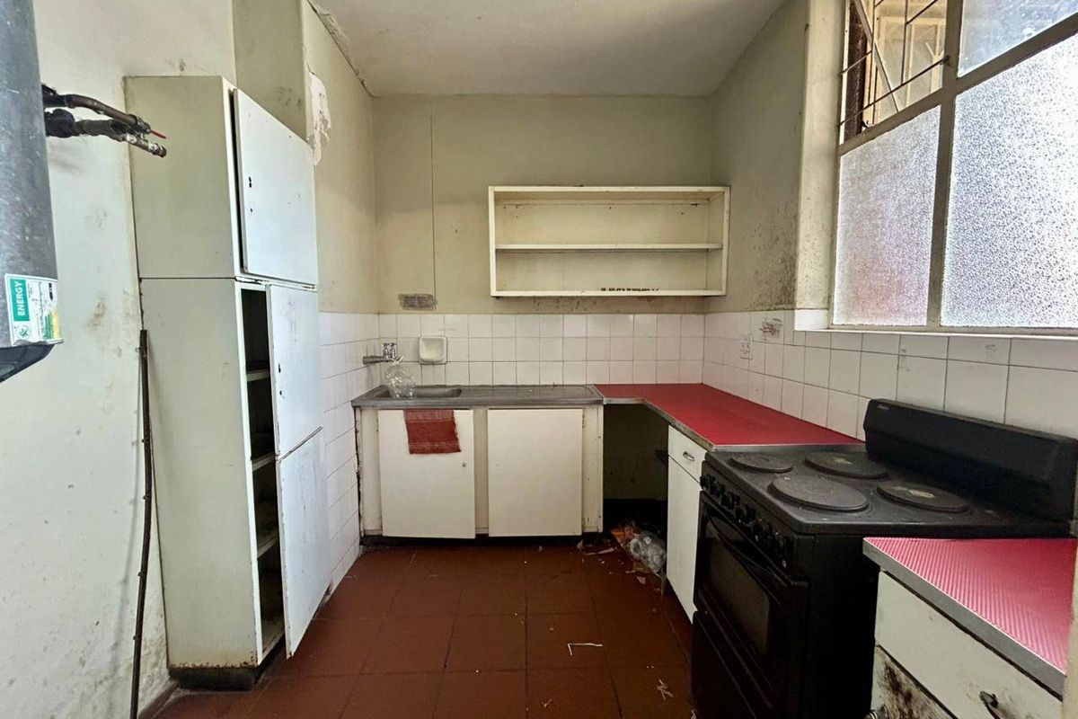 A dated kitchen featuring original cabinetry, a stainless steel sink, and an electric stove, requiring significant renovation and cosmetic updates.