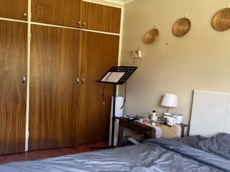 A bedroom featuring built-in wooden cupboards and laminate flooring, offering a functional space with potential for cosmetic updates.