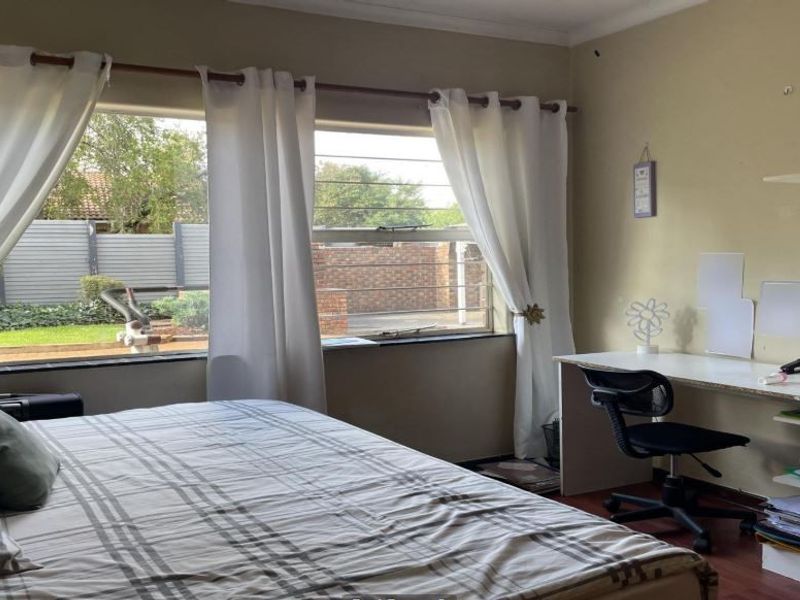 A bedroom featuring a built-in desk and shelving unit, large windows providing natural light, and laminate flooring.