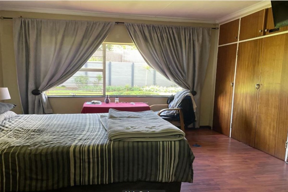 A bedroom featuring built-in wooden cupboards, laminate flooring, and a large window overlooking the garden.