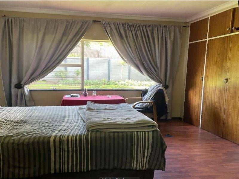 A bedroom featuring built-in wooden cupboards, laminate flooring, and a large window overlooking the garden.