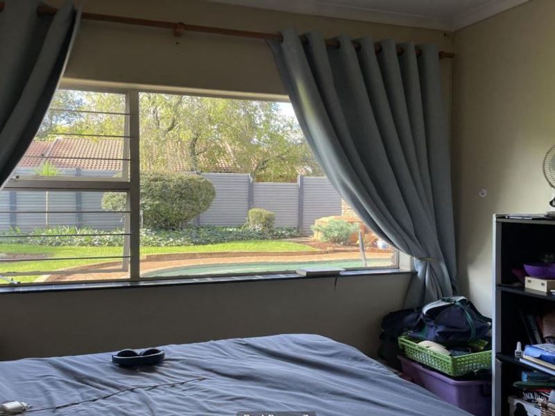 Bedroom featuring a large window with burglar bars, offering a view of the garden and pool area.