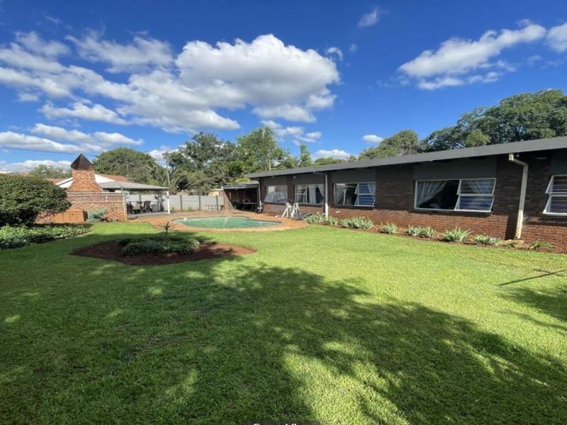 Spacious rear garden featuring a swimming pool, brick facade, and a built-in outdoor fireplace area.