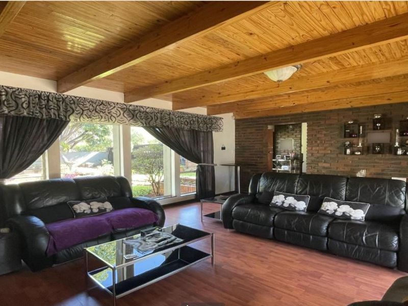 Spacious living room featuring a warm timber beam ceiling, exposed brick feature wall, and large windows providing ample natural light.