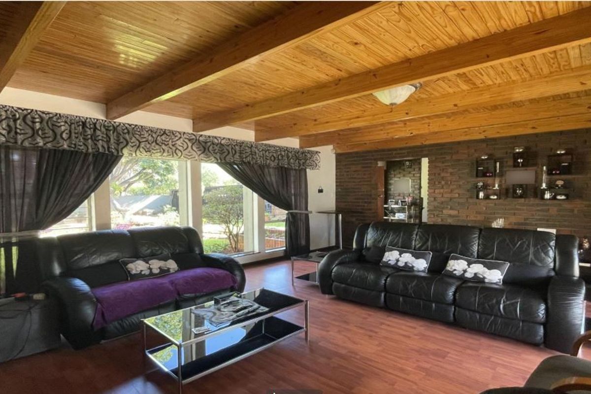 Spacious living room featuring a warm timber beam ceiling, exposed brick feature wall, and large windows providing ample natural light.