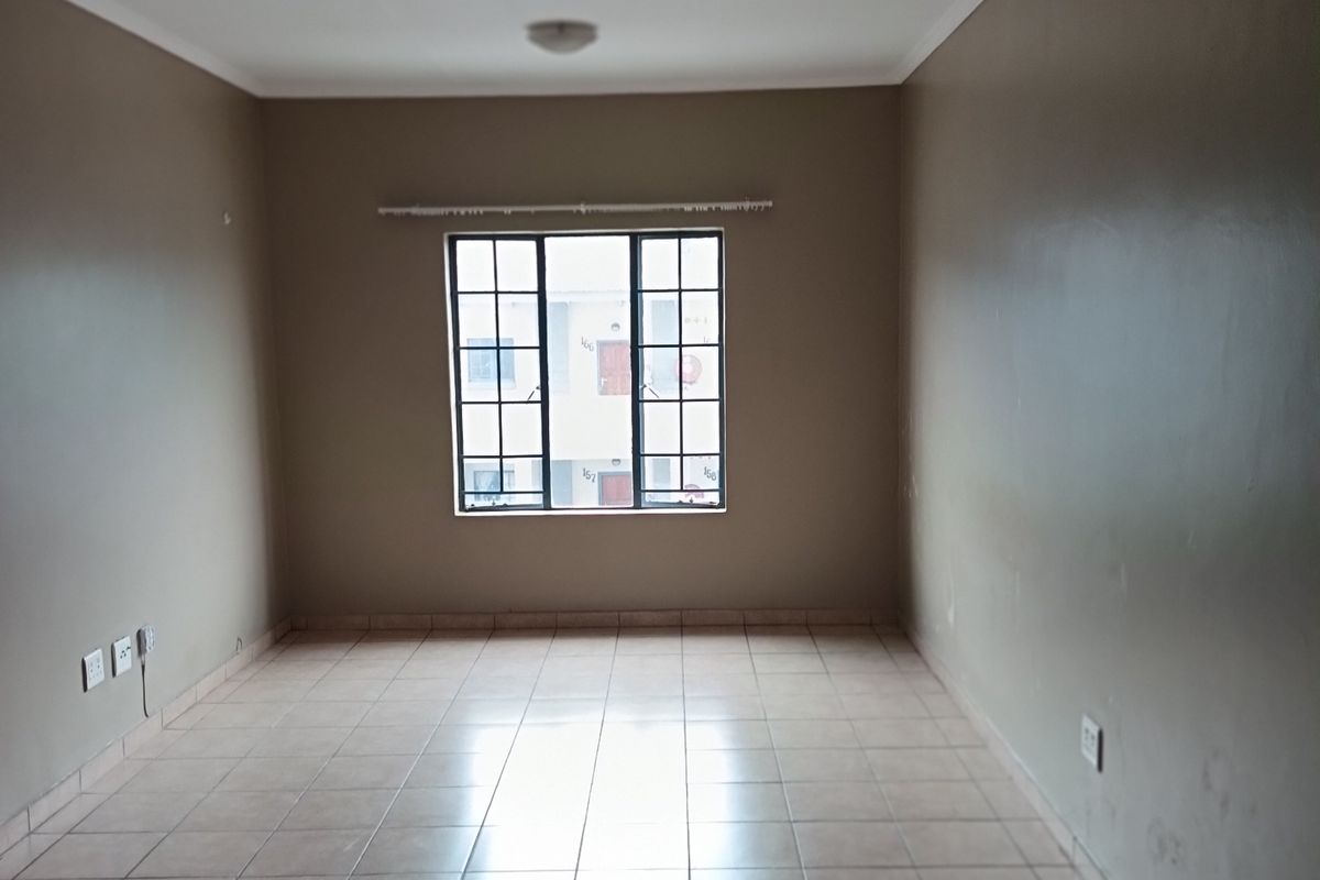 An empty living room featuring neutral-toned walls, tiled flooring, and a grid-pattern window providing natural light.