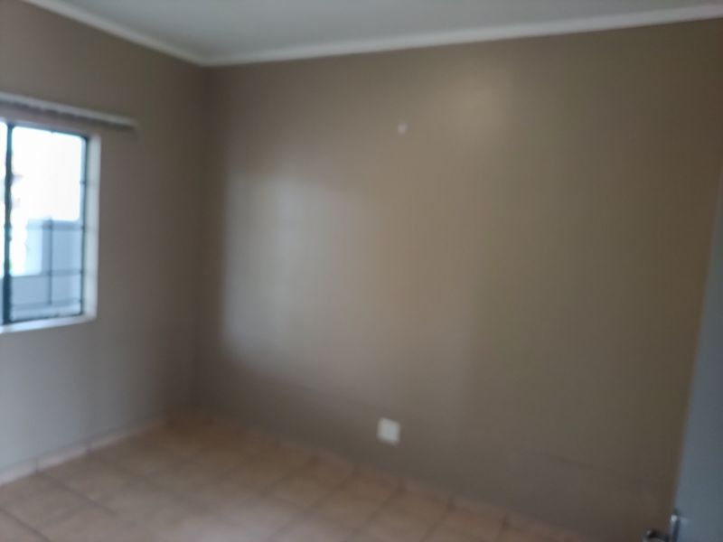 An empty bedroom featuring tiled flooring and a window with security burglar bars.