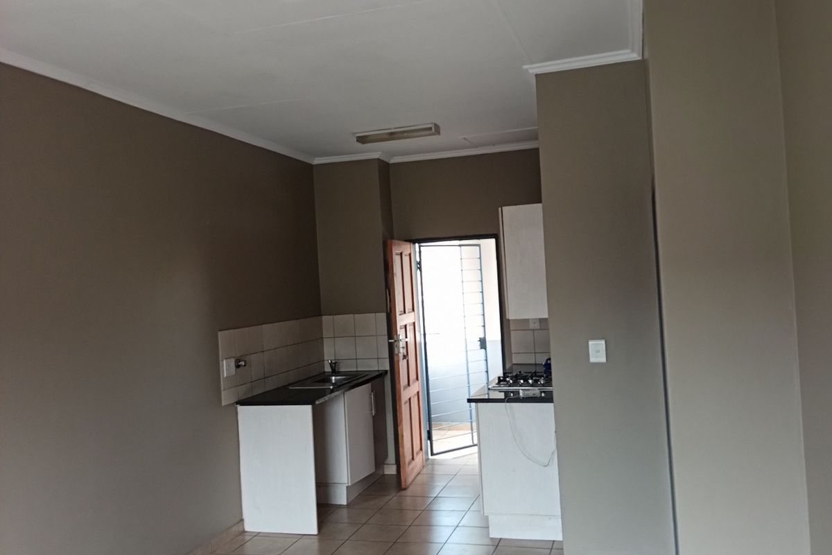 An empty kitchen area featuring tiled flooring, built-in cabinetry with a sink, and a gas hob, leading to an exterior doorway.