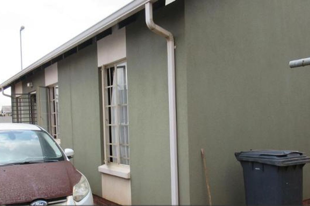 A view of the rear exterior wall of the house, featuring painted plaster finish, guttering, and security bars on the windows.