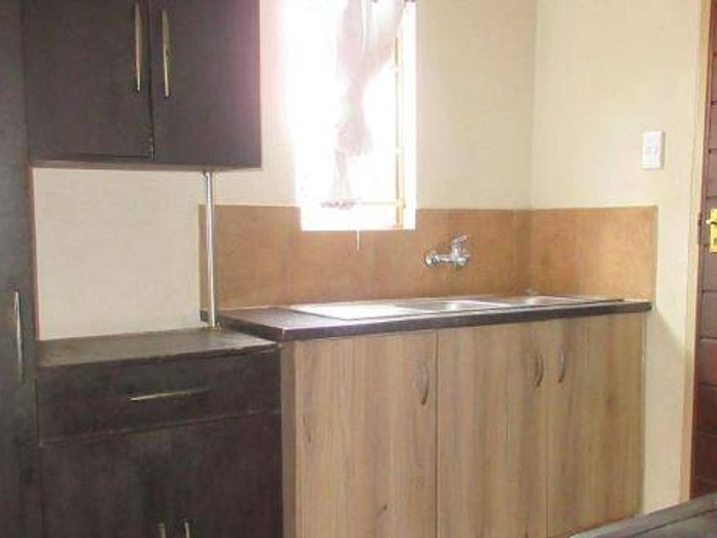 A functional kitchen area featuring built-in cabinetry, laminate countertops, a stainless steel sink, and a tiled splashback.