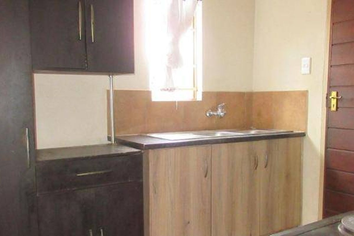 A functional kitchen area featuring built-in cabinetry, laminate countertops, a stainless steel sink, and a tiled splashback.
