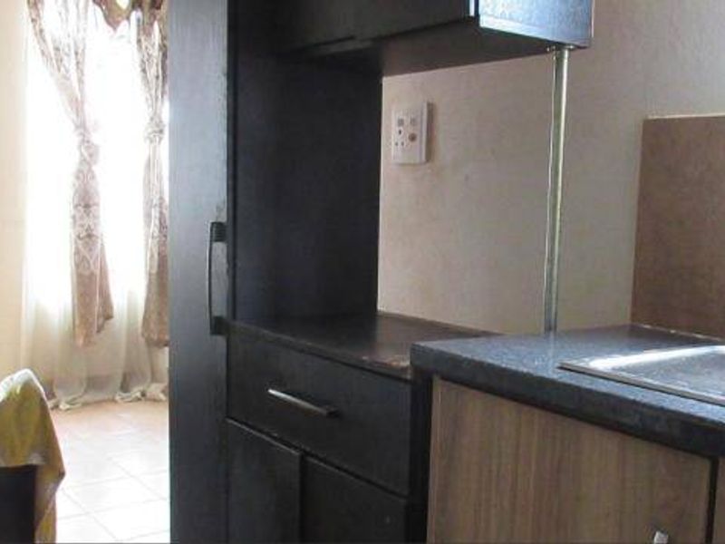 A functional kitchen area featuring built-in cabinetry, laminate countertops, and a stainless steel sink with a tiled backsplash.