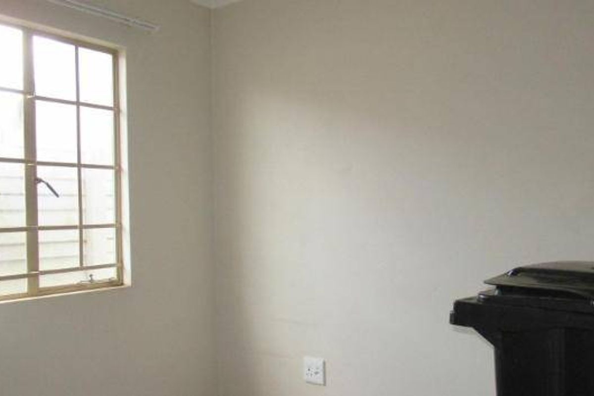 A simple, vacant bedroom featuring a window with security bars and neutral wall finishes.