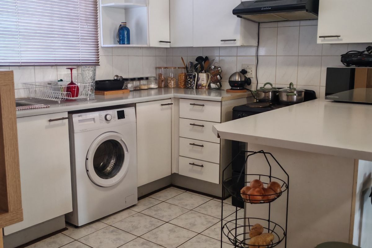 A functional kitchen featuring white cabinetry, tiled flooring, a tiled backsplash, and an integrated washing machine with ample counter space.