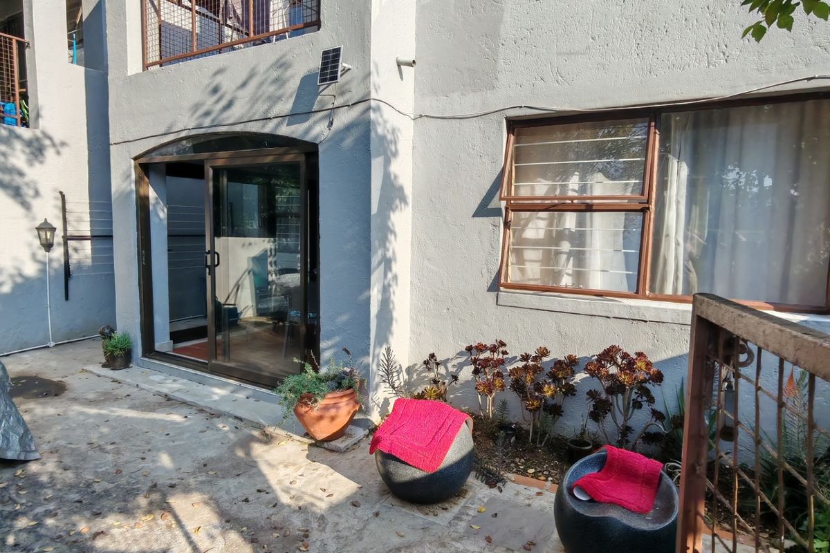 Rear exterior view of the apartment featuring a concrete patio, sliding glass door access, and an upper-level balcony with metal railings.