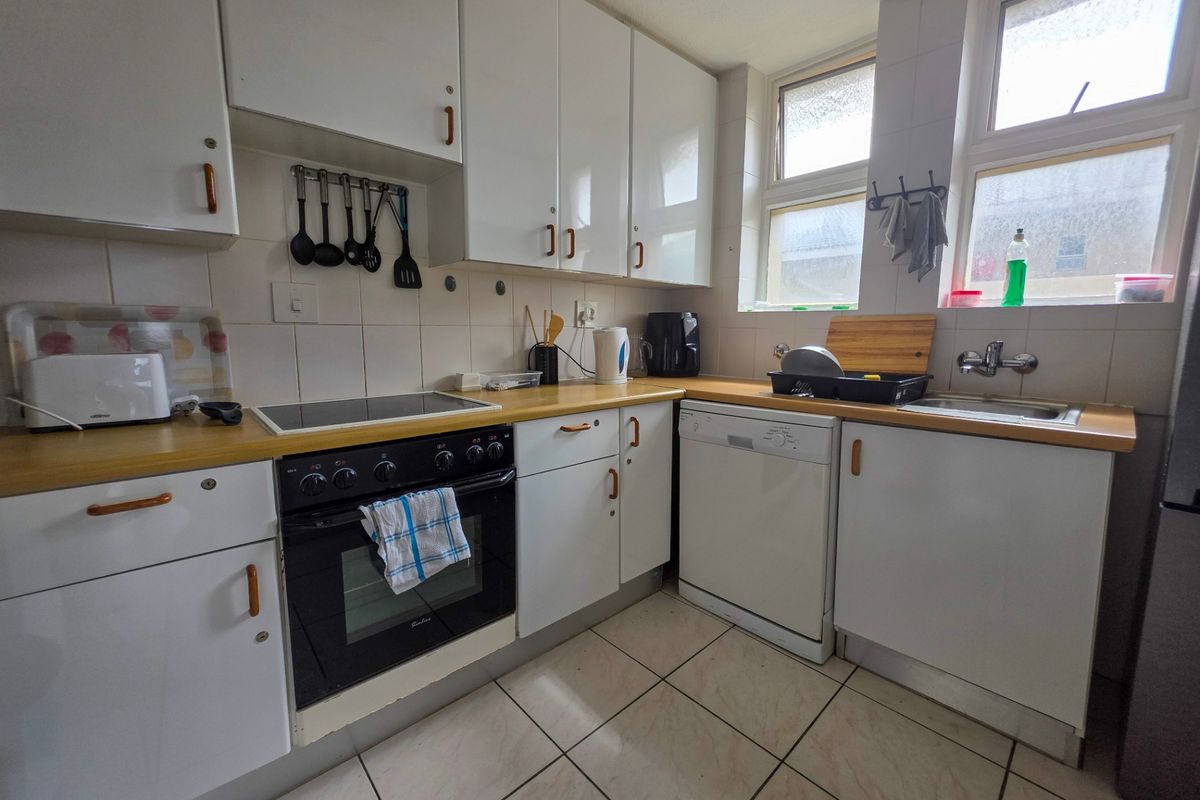 A functional kitchen featuring white cabinetry, laminate countertops, a built-in oven with hob, and tiled flooring, offering a practical layout for daily use.