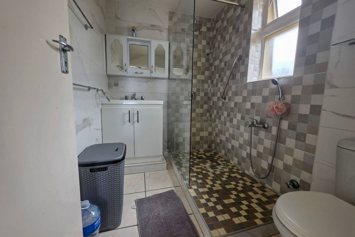 A functional bathroom featuring a glass-enclosed shower, wall-mounted vanity with basin, toilet, and a mix of patterned and marble-effect wall tiling.