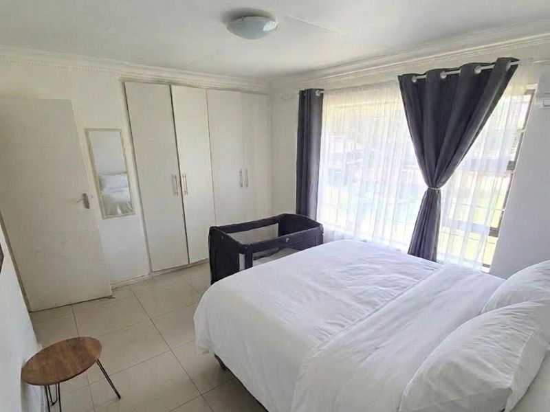 A functional bedroom featuring neutral tiled flooring, built-in storage cupboards, and large windows that provide ample natural light.