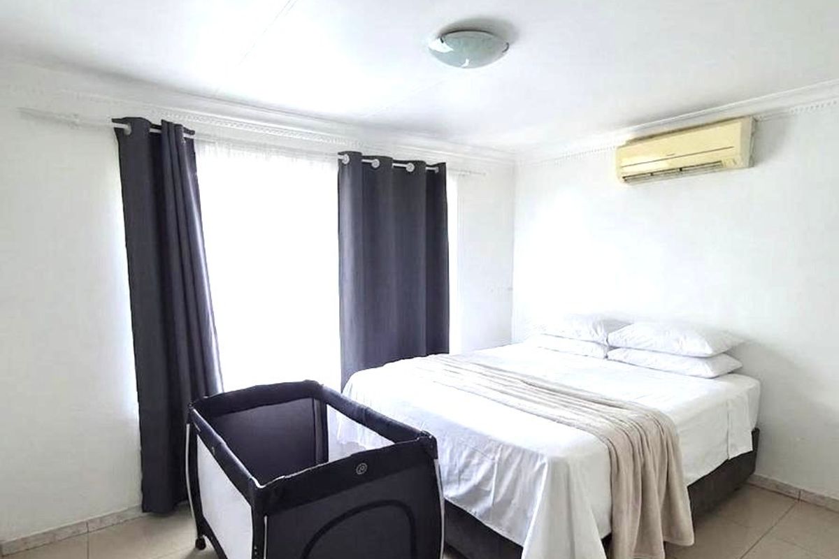 A functional bedroom featuring tiled flooring, a wall-mounted air conditioning unit, and neutral finishes, providing a comfortable and practical living space.