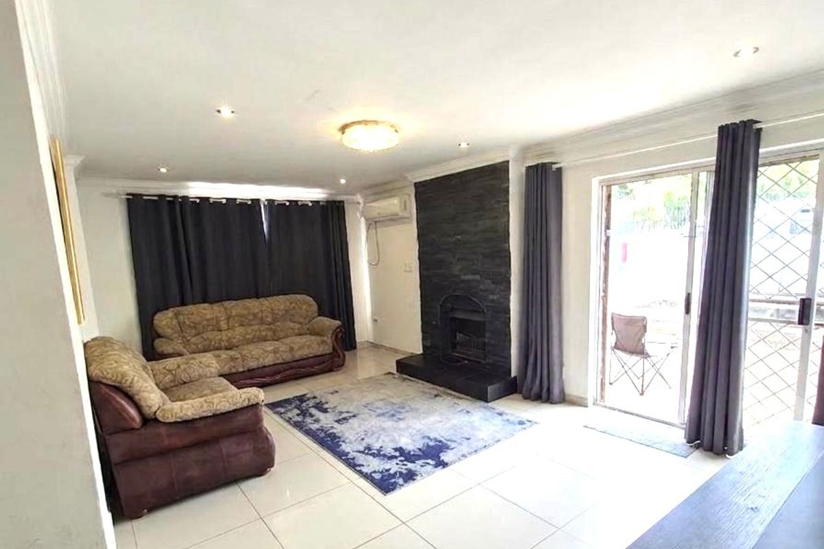 Spacious living room featuring a stone-clad fireplace, large format floor tiles, and direct access to an outdoor patio area through sliding glass doors.