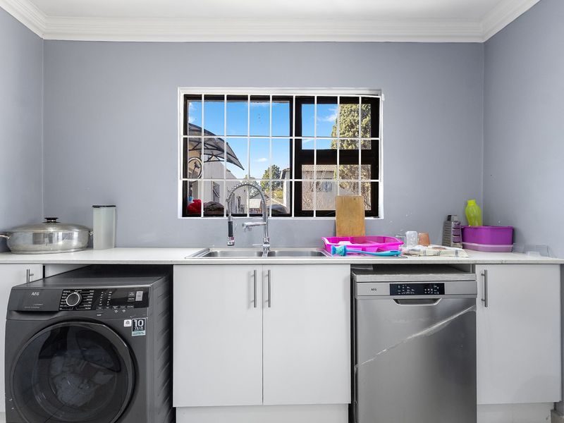 A functional laundry area featuring white cabinetry, a stone countertop, a stainless steel sink with a mixer tap, and a window with security bars.