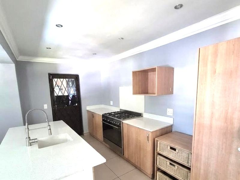 Modern kitchen featuring a central island with quartz countertops, built-in oven, gas hob, and ample cabinetry, finished with neutral tiled flooring.