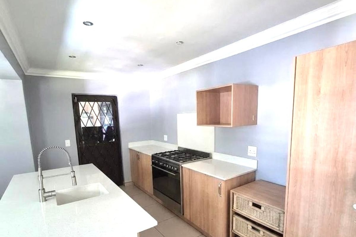 Modern kitchen featuring a central island with quartz countertops, built-in oven, gas hob, and ample cabinetry, finished with neutral tiled flooring.