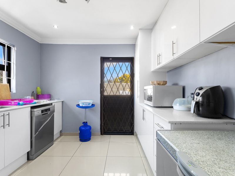 A functional kitchen featuring white cabinetry, stone countertops, tiled flooring, and a secure rear exit door with a security gate.