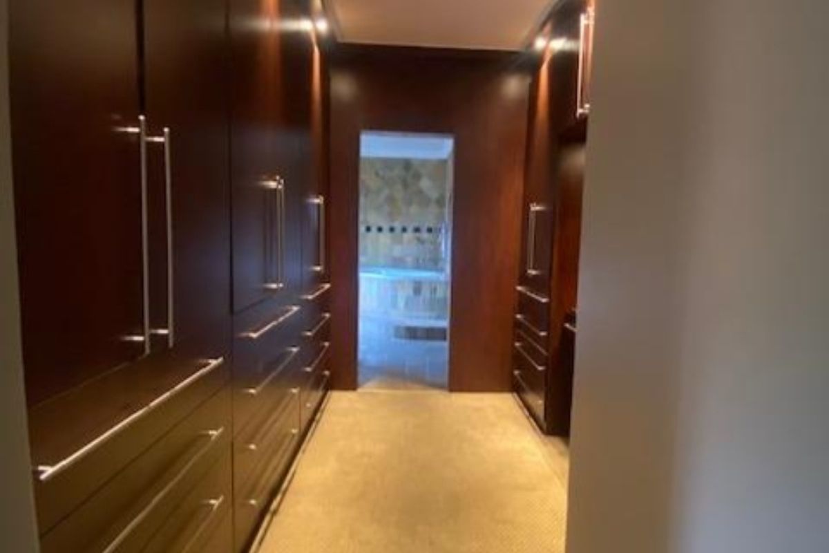 A walk-in dressing area featuring extensive built-in dark wood cabinetry with integrated lighting, leading through to an adjacent bathroom space.