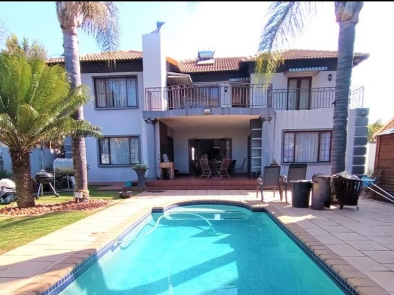 Rear view of a two-story house featuring a swimming pool, paved patio area, and an upper-level balcony with wrought iron railings.