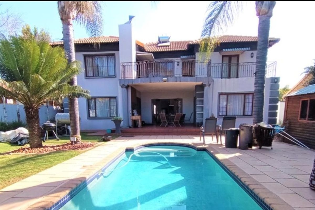 Rear view of a two-story house featuring a swimming pool, paved patio area, and an upper-level balcony with wrought iron railings.