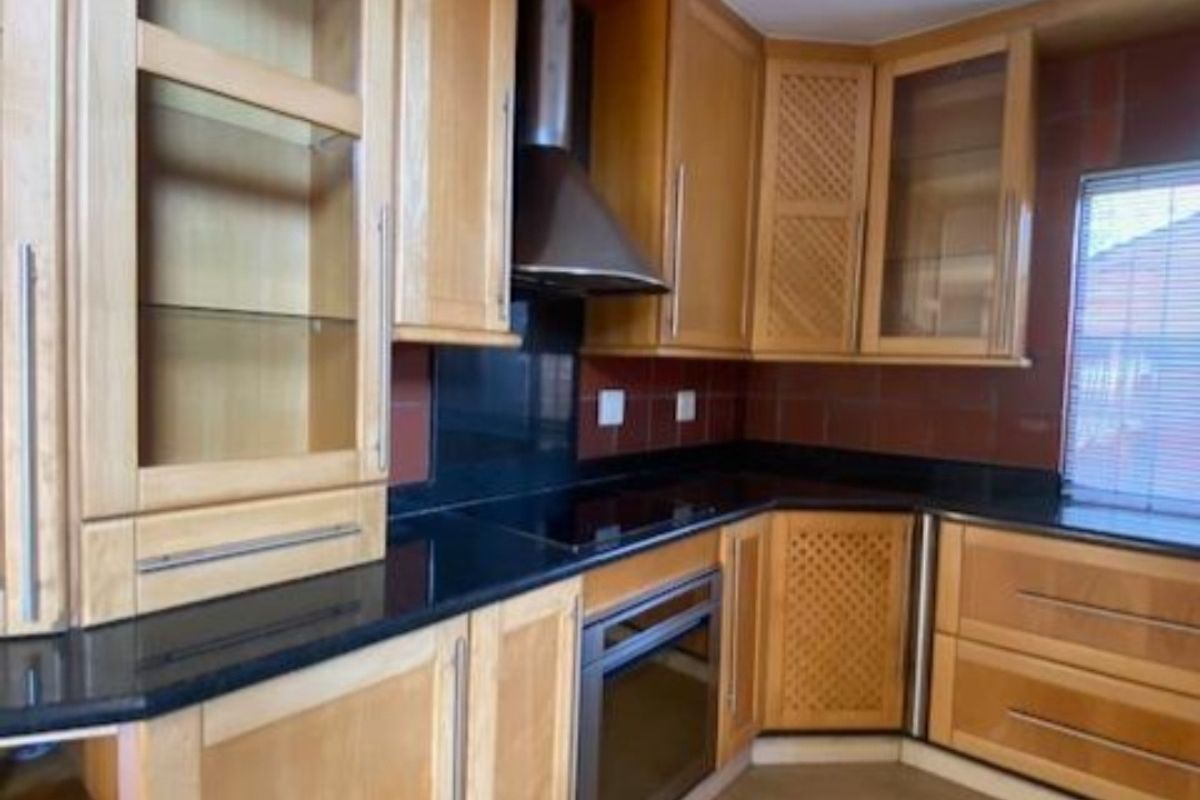 A functional kitchen featuring wooden cabinetry, black granite countertops, a built-in oven, and a stainless steel extractor fan.