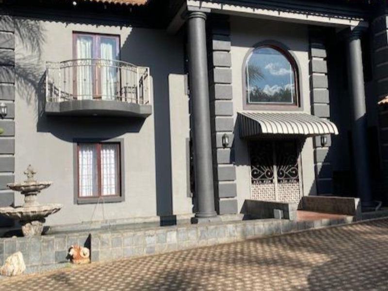Front elevation of a two-story residence featuring a paved driveway, decorative columns, a wrought iron balcony, and a stone fountain.