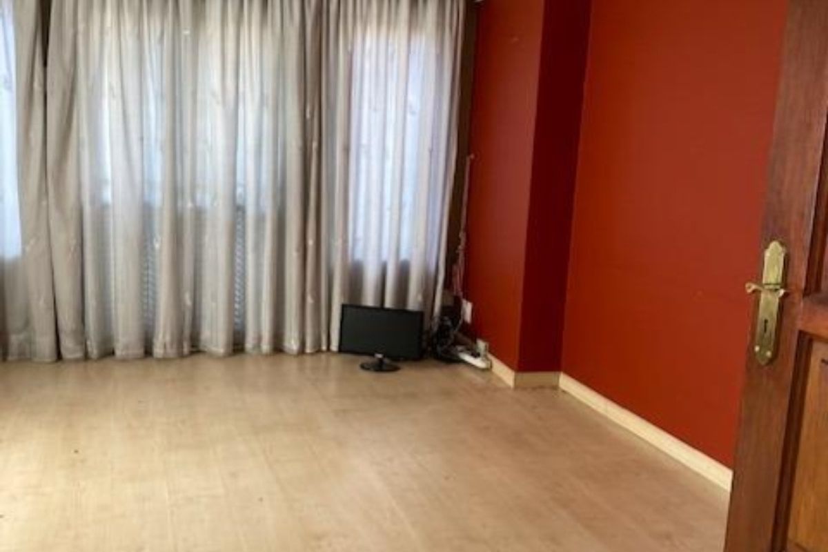 A spacious living room featuring light laminate flooring, crown molding, and a wall-mounted split-system air conditioner.