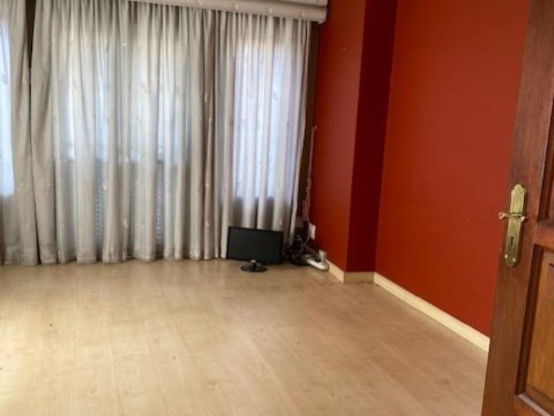A spacious living room featuring light laminate flooring, crown molding, and a wall-mounted split-system air conditioner.