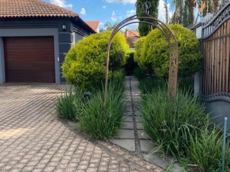 Front exterior view featuring a paved driveway, a garage, and a landscaped garden path with a decorative metal archway.