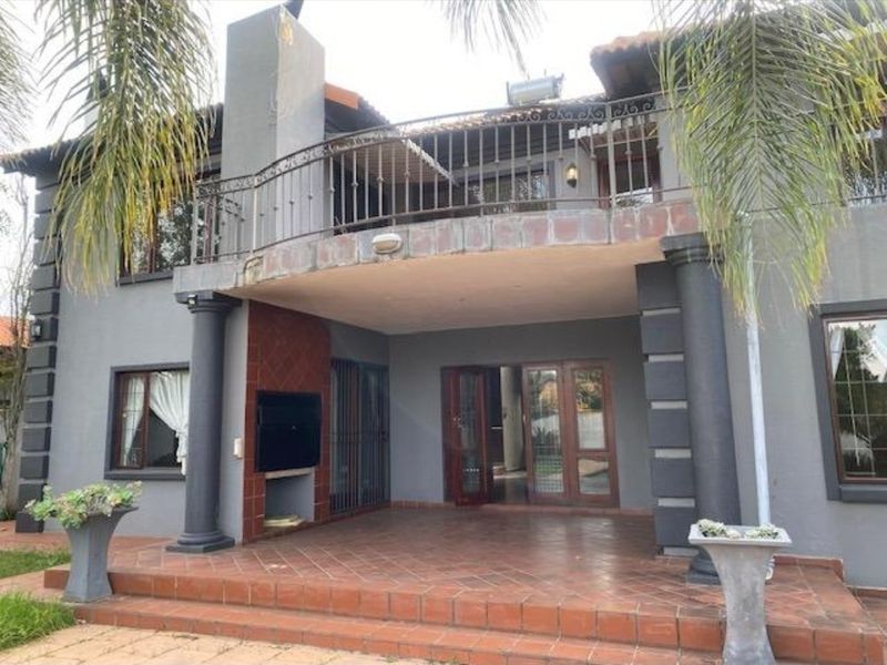 Rear exterior view featuring a covered patio with a built-in braai, terracotta tiling, and an upper-level balcony with wrought iron railings.