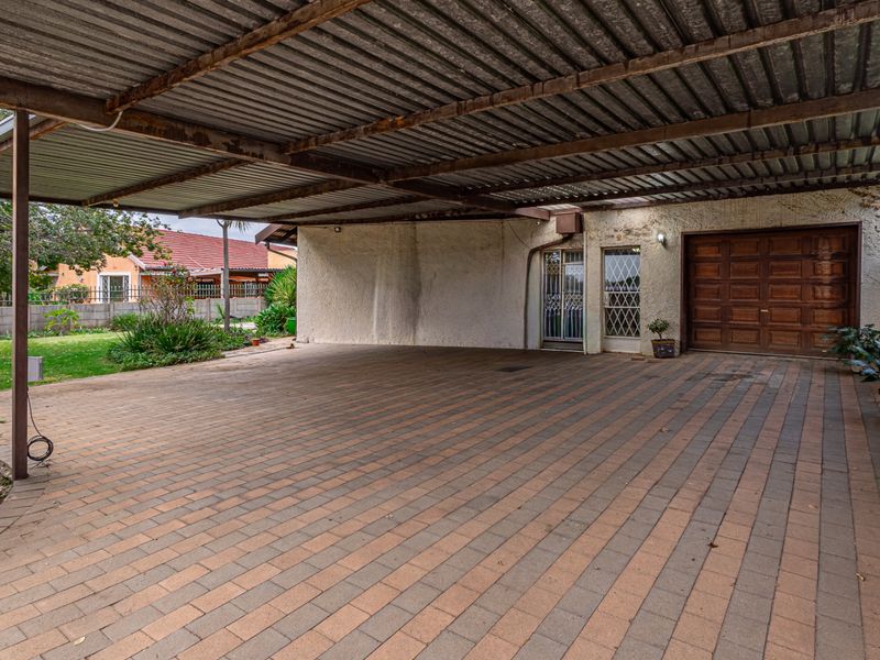 A spacious covered carport area featuring a paved driveway, corrugated metal roofing, and access to a secure wooden garage door.