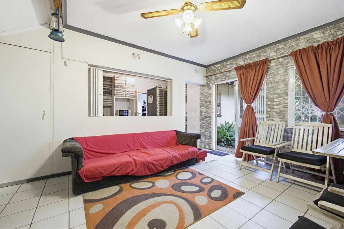 Living room featuring tiled flooring, a ceiling fan, and a serving hatch connecting to the kitchen, with access to an outdoor area.
