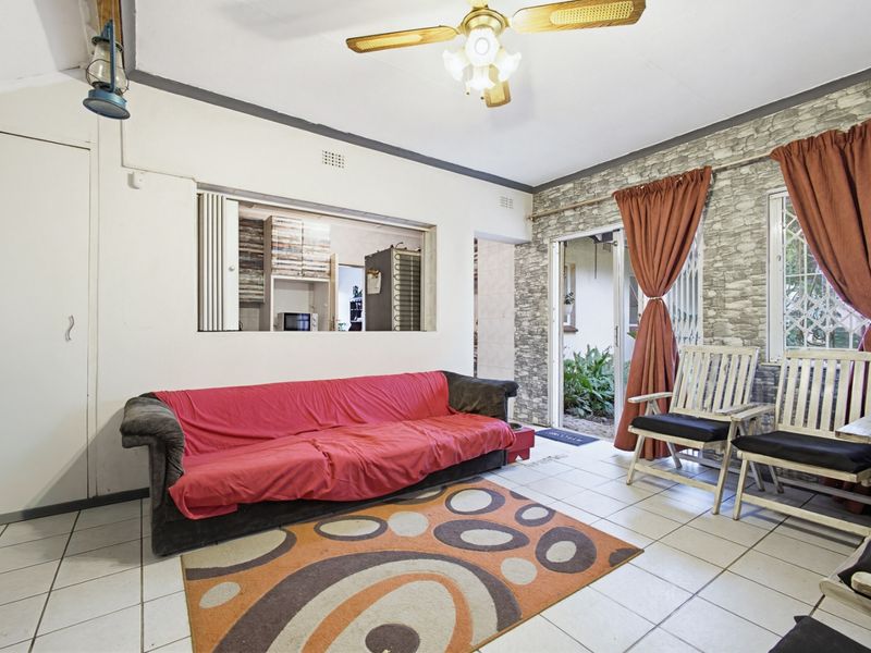 Living room featuring tiled flooring, a ceiling fan, and a serving hatch connecting to the kitchen, with access to an outdoor area.